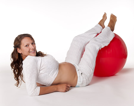 Schwangere macht Gymnastik mit einem roten Ball in der 24. Schwangerschaftswoche